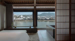Open modern living area with wooden elements, a large window overlooking a river, and a serene atmosphere