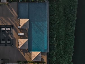 A pool area with four colorful umbrellas providing shade and three chairs for seating, set against a sunny outdoor backdrop