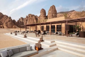 A relaxing outdoor patio area with stone walls, a wooden roof, and comfortable seating arrangements, including chairs and couches