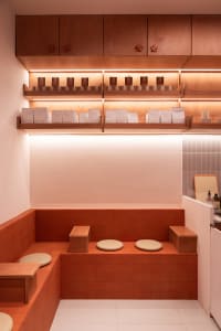 A cluttered orange kitchen with wooden floors and walls, featuring two benches and scattered cups and bottles