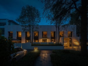 A modern building with a white facade and black accents, featuring multiple windows on a dark night sky
