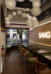 A modern restaurant interior with wooden floors and walls, featuring dining tables, chairs, and potted plants, creating a warm and inviting atmosphere