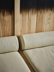 A minimalist living room with two couches, one with a white leather cover and the other made of wood, set against a wooden wall, creating a cozy and comfortable space for relaxation and socializing