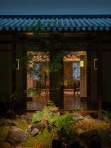 Asian-style house with a tile roof, two doors, potted plants, and chairs in a courtyard