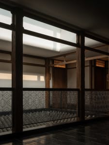 A serene Asian-style hallway with a wooden floor, a staircase, and a bench, set against a backdrop of elegant architecture