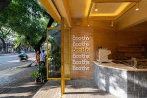 A warm and inviting cafe interior with a yellow wall, white lettering, potted plants, and scattered cups and bowls