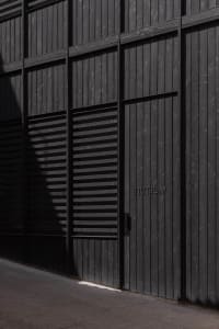 A dark and mysterious exterior building facade with a black door and a white sign, set against a dimly lit background