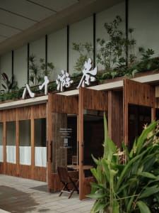 Warm and inviting Asian restaurant with wooden walls, a large window, and potted plants, featuring a dining table and comfortable seating