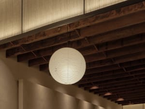 A minimalist room with wooden walls and floors, featuring a large white light fixture suspended from the ceiling, with a sense of emptiness and minimalism
