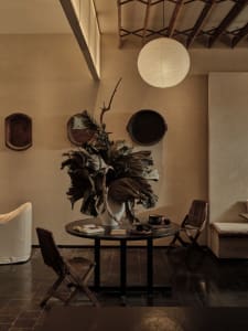 A warm and inviting dining room with a large table surrounded by chairs, a smaller table, and a vase with leaves as a centerpiece, featuring wood elements and a cozy atmosphere