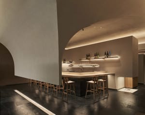 A cozy restaurant bar with a wooden countertop, chairs, and bottles on display, creating a warm and inviting atmosphere