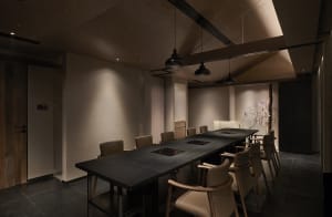 Empty restaurant with a long wooden dining table surrounded by leather chairs and potted plants, creating a cozy atmosphere