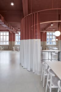 Modern restaurant interior with red and white walls, multiple dining tables, and chairs, featuring clean lines and minimalistic design elements