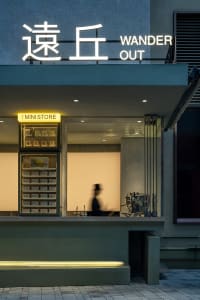 A modern storefront with a glass front, visible interior, and a man walking past carrying a handbag in a lively urban environment