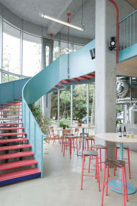 Modern living area with a spiral staircase, dining table, potted plants, and decorative bottles, featuring a mix of red and blue hues