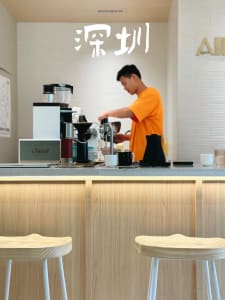 A man prepares coffee in a kitchen with a coffee maker, cups, and bowls, surrounded by a casual atmosphere