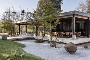 A relaxed outdoor dining area with a patio featuring multiple benches and chairs, surrounded by trees and perfect for al fresco meals