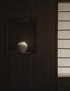 A dimly lit bathroom with a wooden cabinet featuring a white vase, creating a calm and serene atmosphere