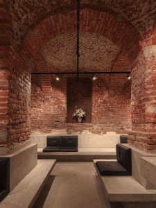 Modern interior design concept featuring a brick building with a stone archway, black couches, and a decorative vase in a large open area