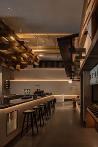 Modern restaurant interior with a bar area, dining tables, wood, and metal elements, warm lighting, and potted plants
