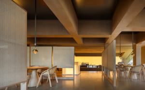 Open living area with wooden floors and walls, featuring a dining table, chairs, refrigerator, sink, and microwave, with a modern and contemporary design