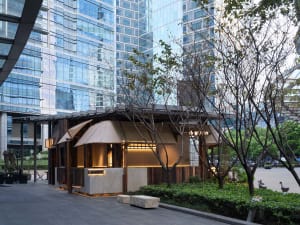 Cozy outdoor cafe with a wooden shelter, dining table, and chairs, situated in front of a tall building with a motorcycle parked nearby