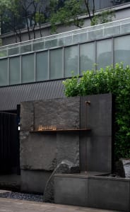 A modern building with a stone wall and metal pipe, surrounded by potted plants, conveying a sense of functionality and design