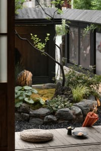 Serene garden area with a rock wall, potted plants, and a tree, featuring natural elements and inviting atmosphere