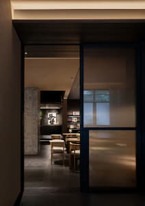 Dining area in an Asian restaurant with dark wood elements, potted plants, artwork, and warm lighting