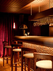 A cozy bar area with a long wooden counter and stools, wine glasses, and a warm atmosphere