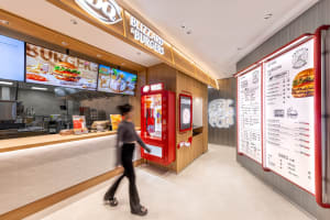A restaurant interior with a wooden theme, featuring a counter, menu board, and soda machine, with two people in the scene, well-lit and inviting