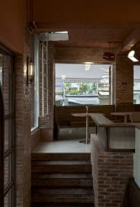 Modern restaurant interior with brick walls, a wooden countertop, and dining tables near windows, featuring a warm and inviting atmosphere