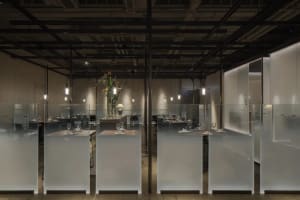 A modern restaurant with a large dining area featuring multiple tables and chairs, wine glasses, and a clean, well-organized atmosphere