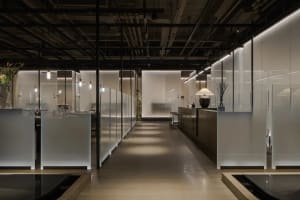 A modern restaurant with a long hallway lined with glass walls, featuring chairs placed throughout the space, creating a clean and well-lit atmosphere
