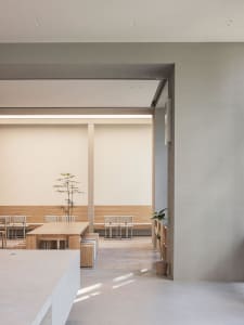 A modern restaurant interior with a large dining table, gray walls, and comfortable seating for a calm and inviting atmosphere
