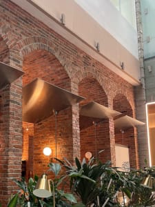 A warm and inviting interior space with brick walls, arches, columns, potted plants, and comfortable seating