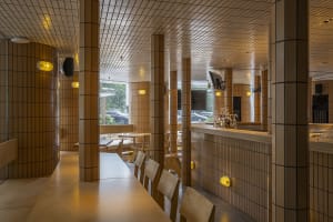 Dining area with a bar counter, wooden furniture, and white table tops, creating a warm and inviting atmosphere