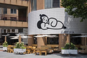 An Asian restaurant with a unique exterior design, featuring wooden tables and chairs, umbrellas, and an inviting atmosphere for outdoor dining