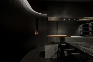Industrial kitchen with a large stove top oven, black walls and floors, and a dining table with chairs