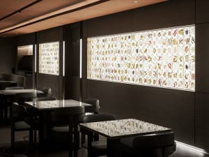 Dimly lit restaurant with multiple tables and chairs, glass walls, and natural light from a large window