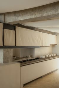 Empty kitchen with white walls and cabinets, featuring bowls, cups, and vases on countertops in a clean and minimalistic atmosphere
