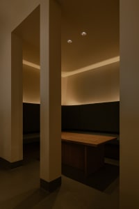 Dimly lit room with a wooden table and two benches, surrounded by white walls and a simple atmosphere