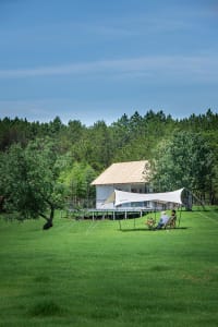 Two people sitting on chairs under a canopy tent in a peaceful green grassy area with a small house nearby