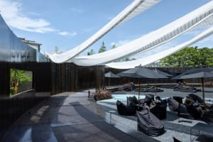 Outdoor patio with seating areas, umbrellas, a pool, and trees in the background