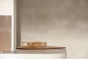A wooden architectural model of a modern building on display, showcasing clean lines, windows, doors, and structural components, with highlighted intricate details and craftsmanship