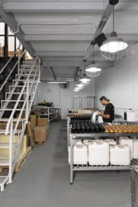 Industrial kitchen with a counter filled with various items, multiple clocks on the wall, and a man standing in the background