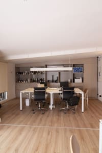 A modern office space with a large white table surrounded by multiple chairs on a wooden floor, creating a warm and inviting atmosphere