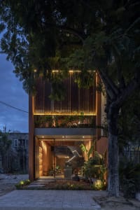 A modern house with a large window, surrounded by potted plants and two chairs, set against a natural background
