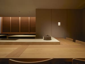Empty kitchen with wooden floors and walls, featuring two dining tables and a chair, with a calm and inviting atmosphere