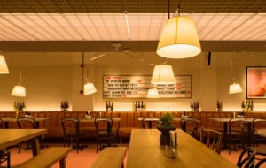 Modern restaurant interior with wooden floors, neutral-toned walls, and tables and chairs, with bottles and a bar